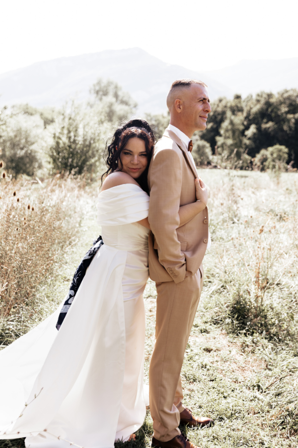 Couple de mariés, robe blanche et costume beige, dans un champ, ambiance bohème et lumière d'été