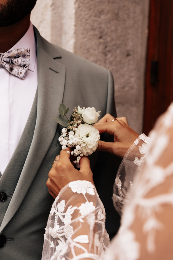 Mariée qui attache des fleurs sur le costume du marié.